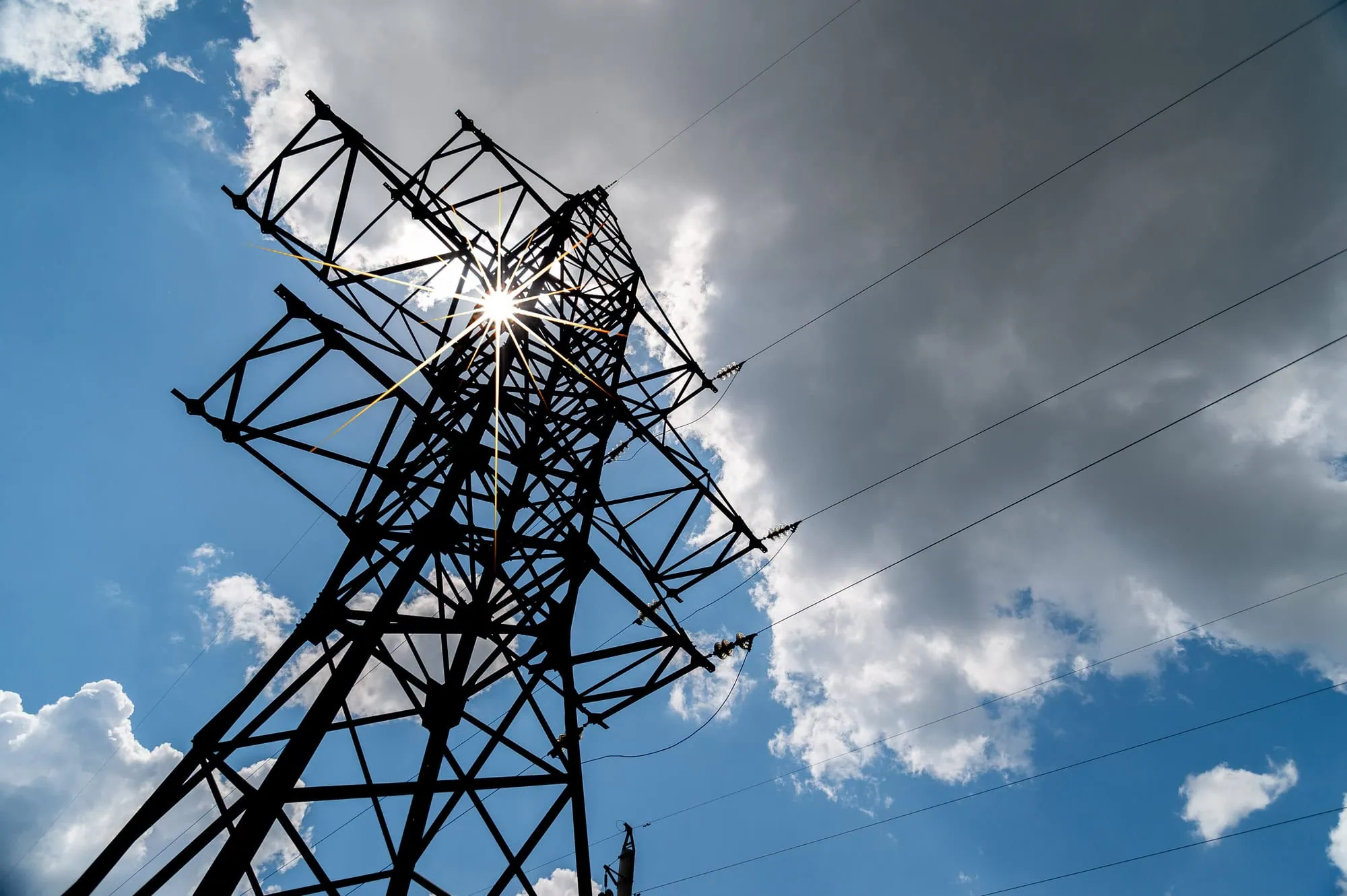 an electric utility tower and lines against a partly cloudy sky.