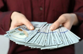 a person fans out numerous hundred dollar bills.