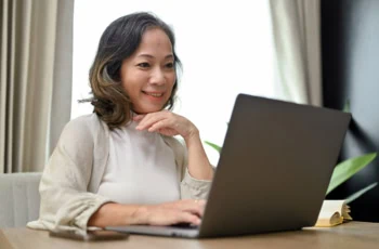 a middle-aged woman smiles while viewing her laptop.