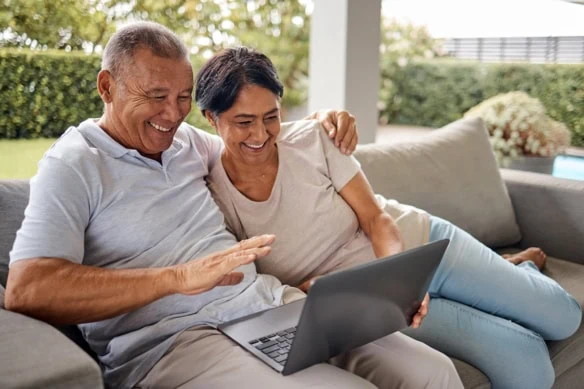 an older couple smile while looking at a laptop.