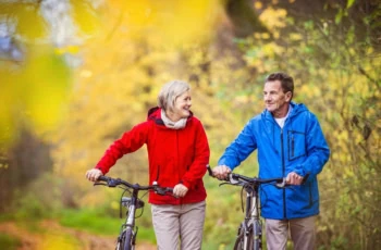an older couple walk their bikes along a path.
