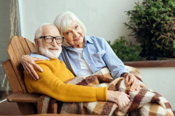 an older couple sits together under a blanket.