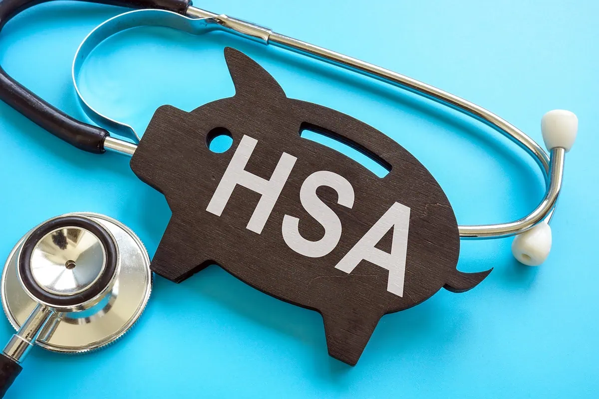 The "Stealth IRA": How to Retire Early Using Your HSA 2 a stethoscope wrapped around a flat wooden piggy bank carving that says H S A.