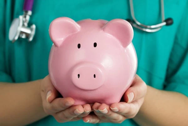 a nurse in green scrubs holds a pink piggy bank.