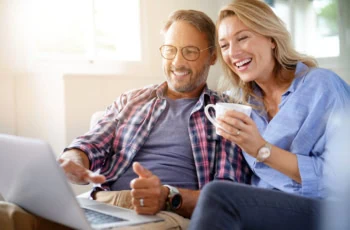 a mature couple sits and smiles while looking at a laptop.
