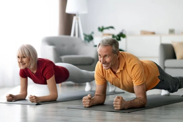 Cheerful athletic mature couple working out in their living room.