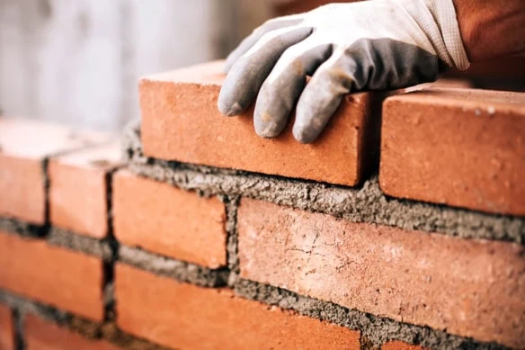 a bricklayer sets a brick into mortar.