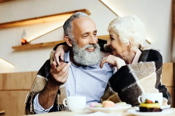 an older couple cuddles on the couch under a shawl.