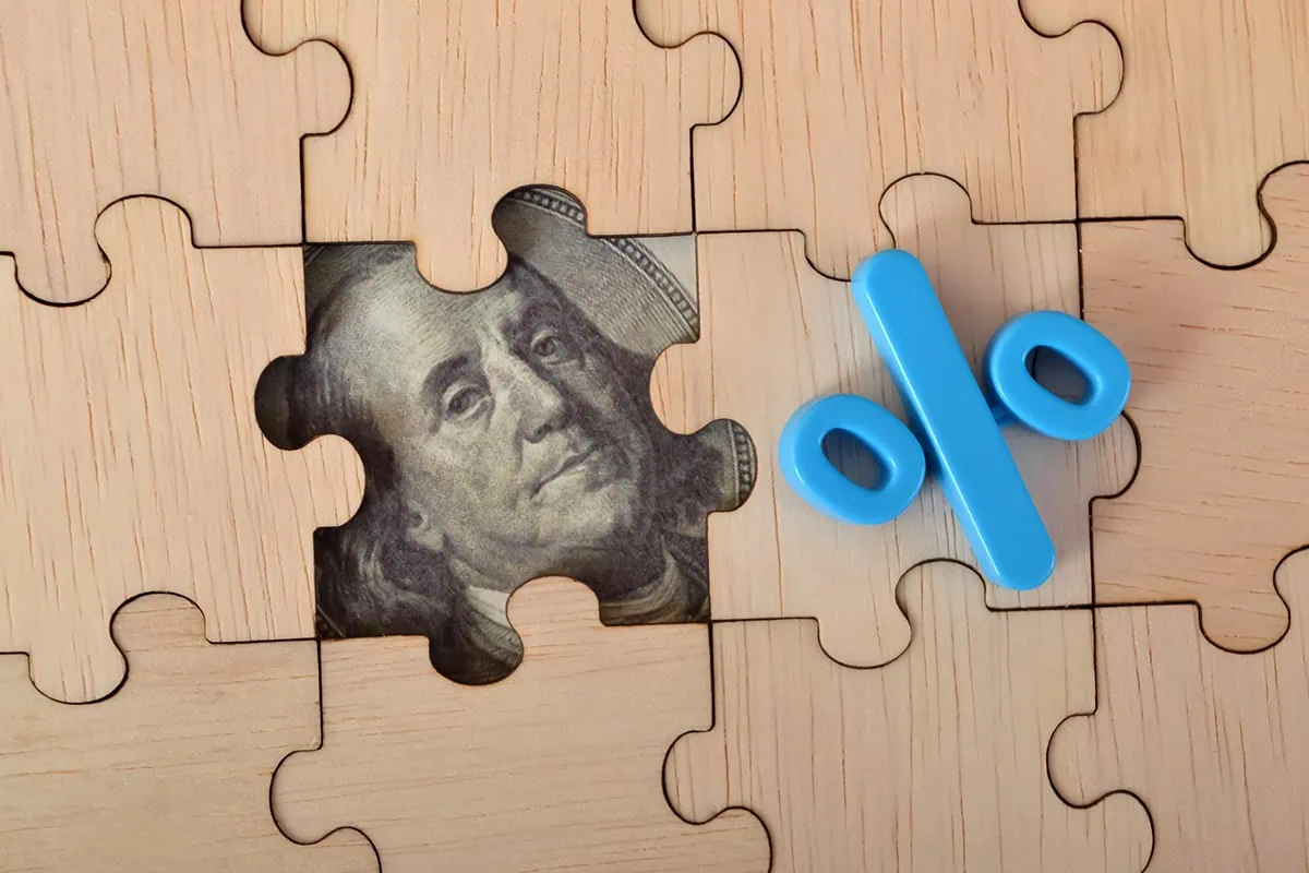 concept art of a puzzle piece removed revealing part of a dollar bill and a percent sign sits atop the puzzle indicating yield.