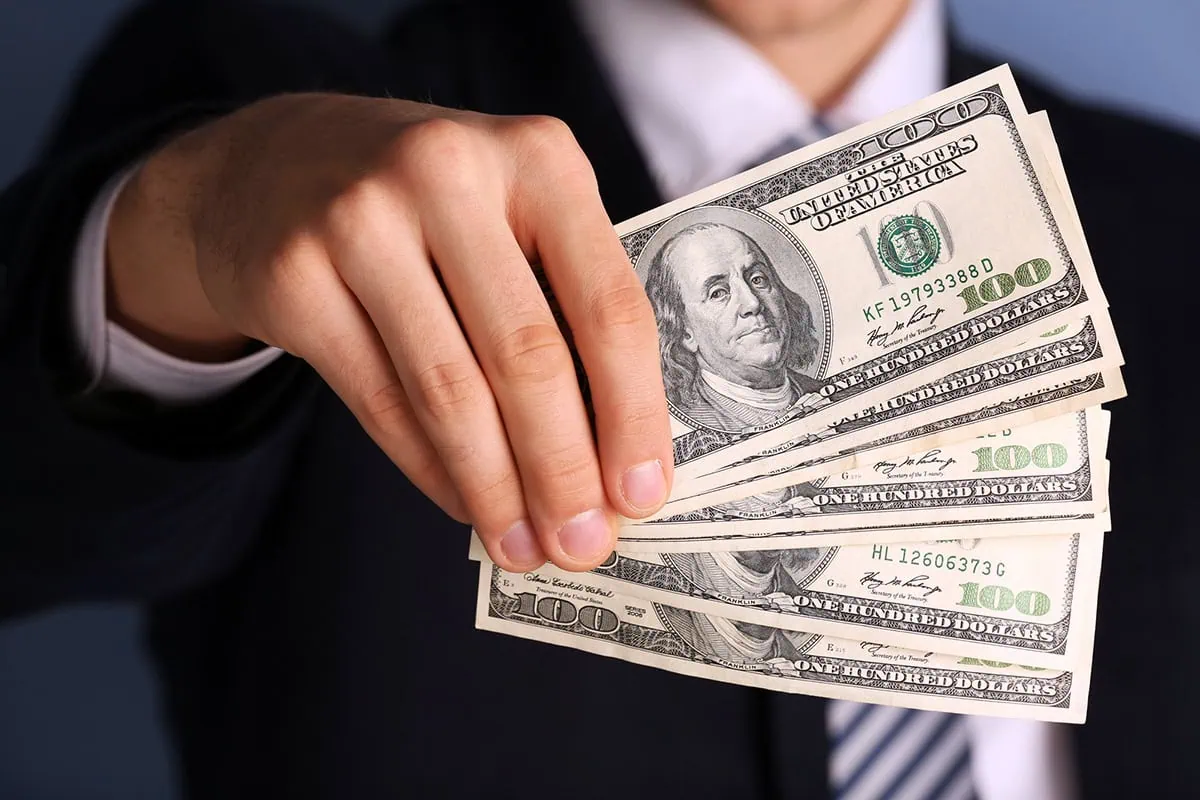 a businessman holds several hundred dollar bills in front of him.
