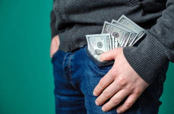 a man wearing jeans has many hundred dollar bills spilling out of his pants.