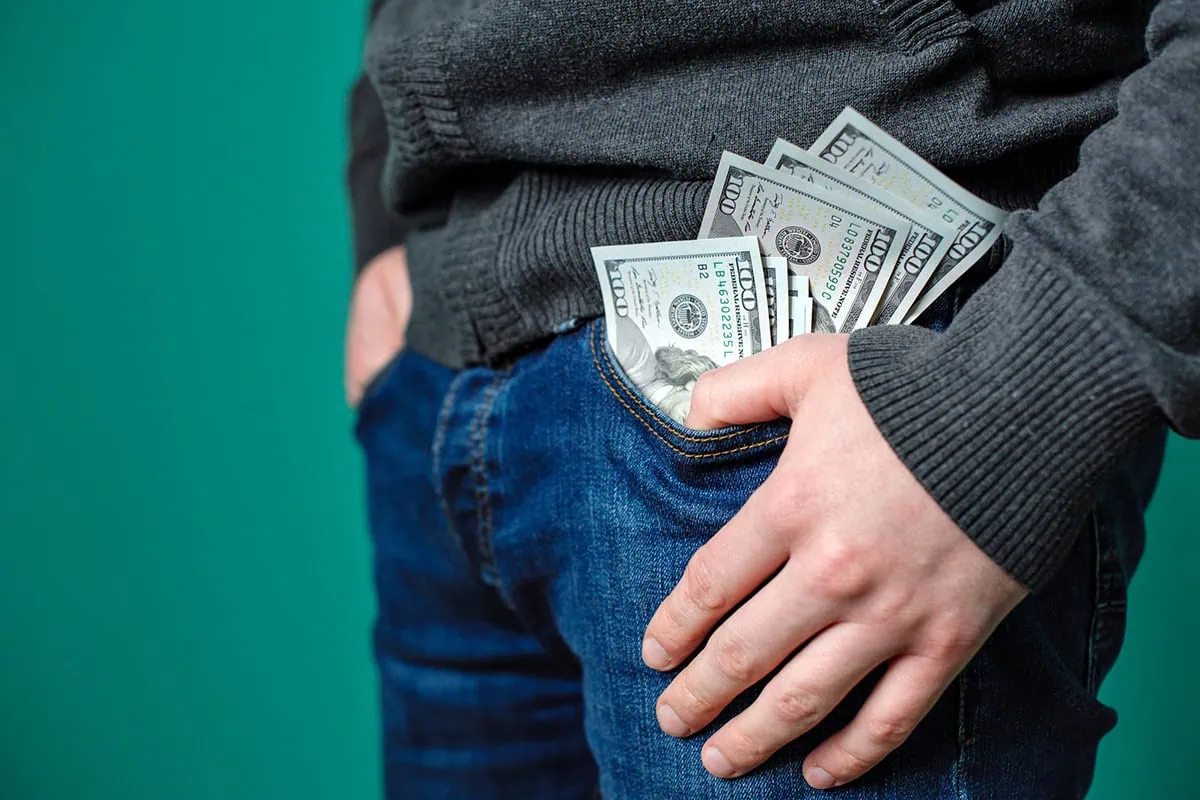 Your Parents' Financial Playbook Is Outdated: Skip These Tidbits of Monetary Advice 2 a man wearing jeans has many hundred dollar bills spilling out of his pants.