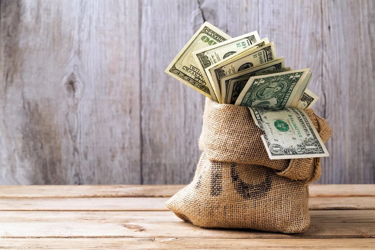 money in a sack sitting on a wooden table.