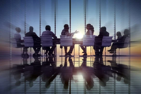 a group of business executives sit around a table during a meeting.