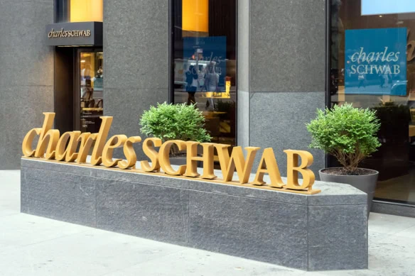 the charles schwab logo in three dimensional gold letters sits on a long concrete slab.