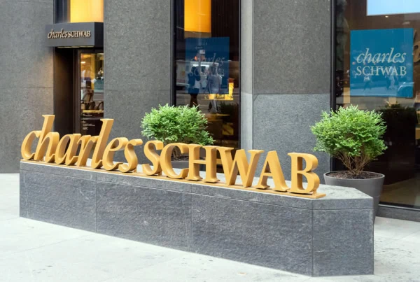 the charles schwab logo in three dimensional gold letters sits on a long concrete slab.
