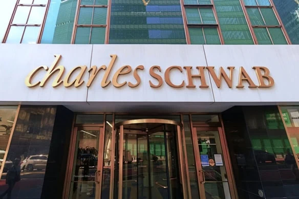 a gold charles schwab sign against a white background on a city building.