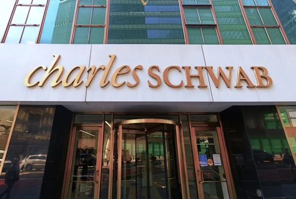 a gold charles schwab sign against a white background on a city building.