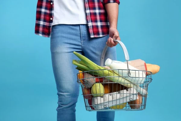 a man carries a grocery basket against a blue background.