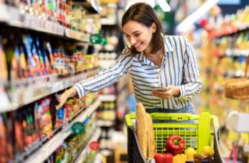 a woman grabs groceries off the shelf in a store aisle.