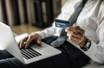 a man holds a credit card while using his laptop.