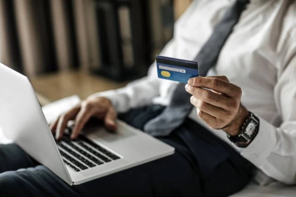 a man holds a credit card while using his laptop.