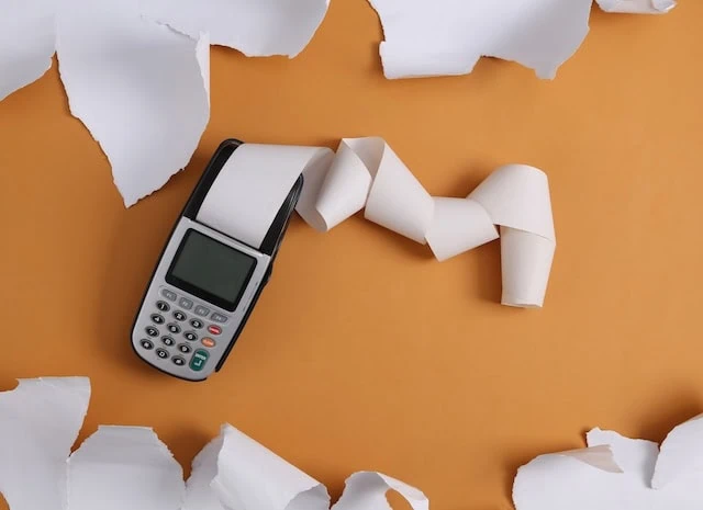 Payment terminal and white torn paper sheets on beige background