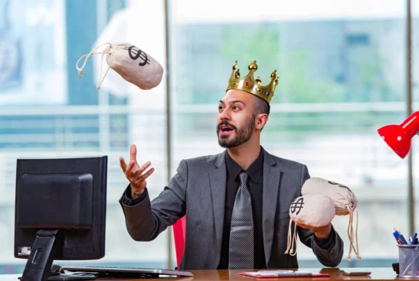 a businessman wearing a kings crown juggles little cloth bags of cash.