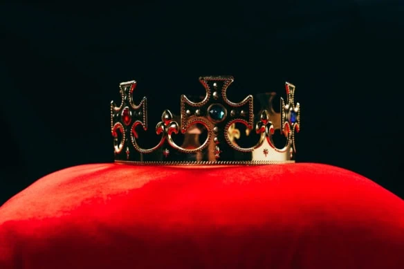 a kings crown rests on a red pillow.