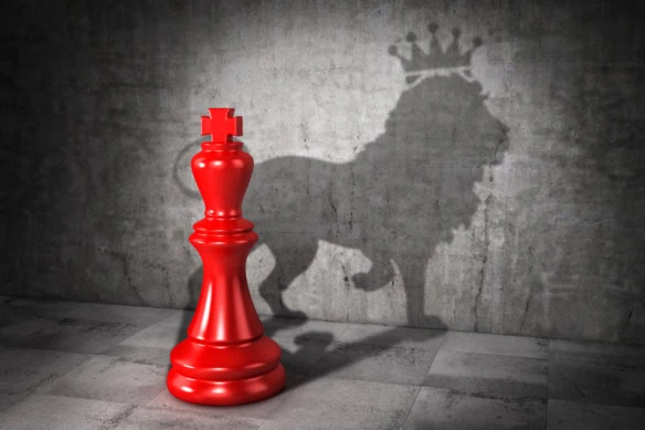 A red chess king casts a shadow of a lion against a gray wall.