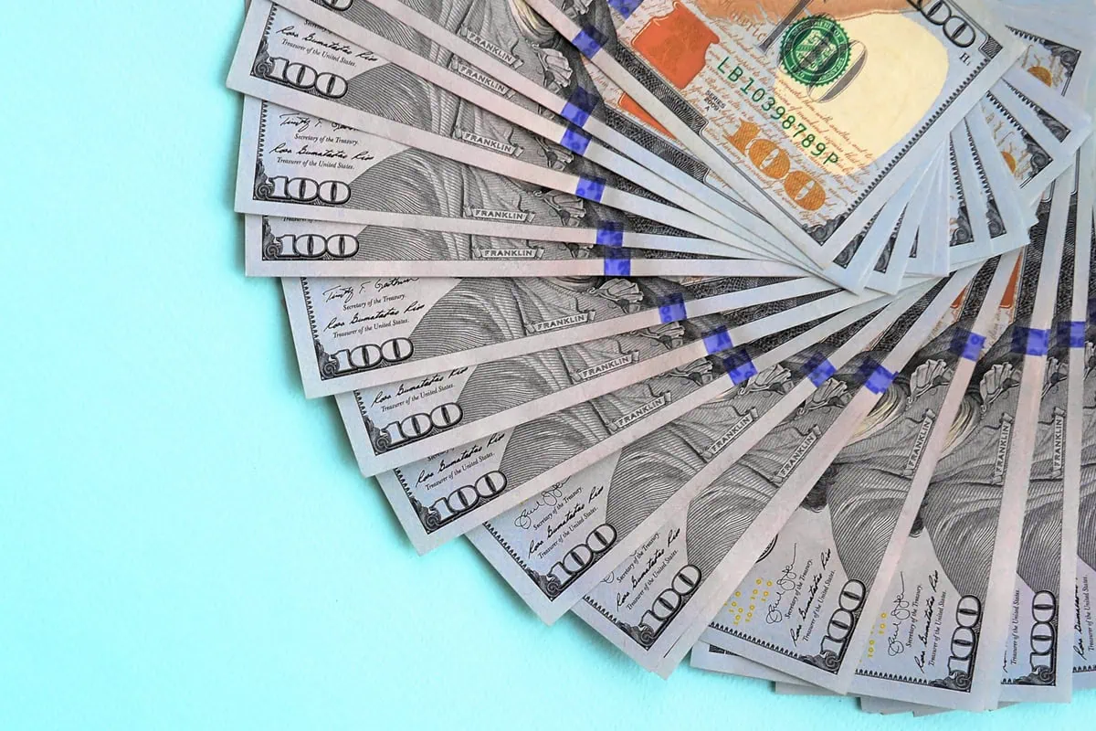 a fan of hundred dollar bills against a blue background.