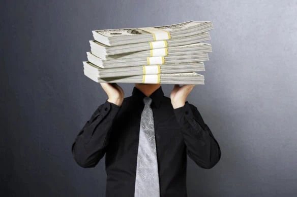 a man tries to lift stacks of comically large hundred dollar bills over his head.