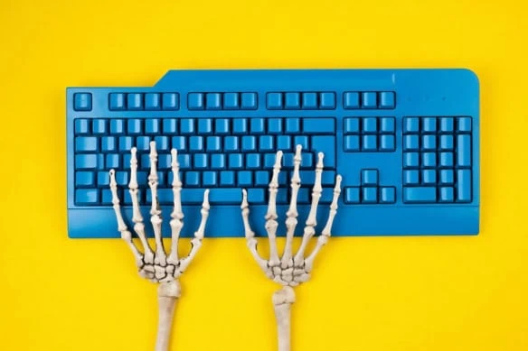 Human skeleton hands typing on blue computer keyboard, flat lay, top view.