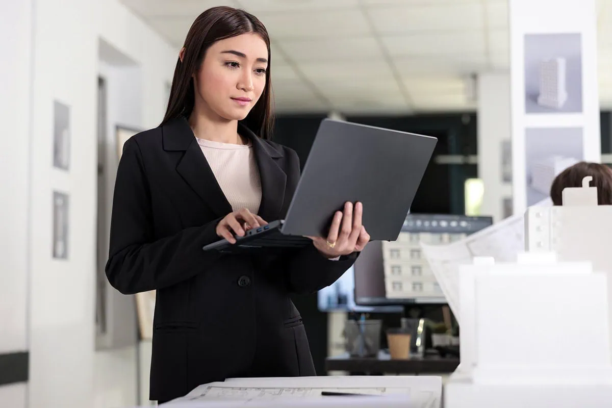 The Tariff Ripple Effect: What It Means for the Corner Store and Beyond 2 A young architect holds her laptop while standing.