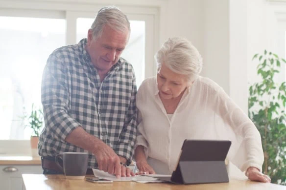 elderly couple looking at documents and a tablet together in the kitchen