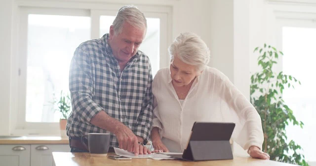 elderly couple looking at documents and a tablet together in the kitchen