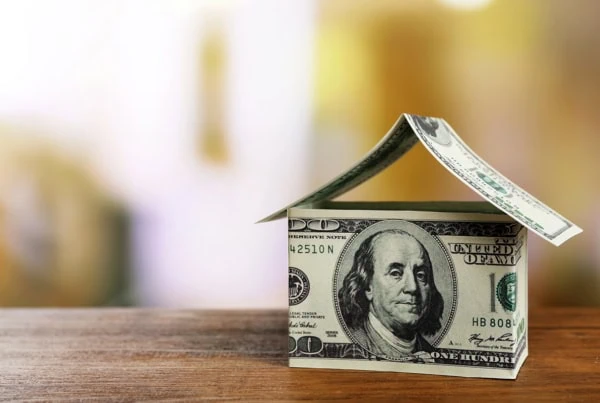 a small house made out of a few hundred-dollar bills sits on a wooden table.