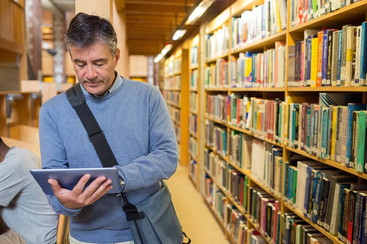8 Tips to Improve Your Financial Literacy 3 A middle-aged man reading a book while walking in the library.