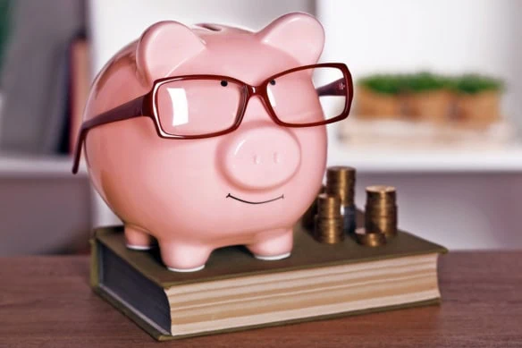 A piggy bank with glasses standing on a book.
