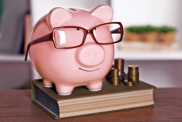 A piggy bank with glasses standing on a book.