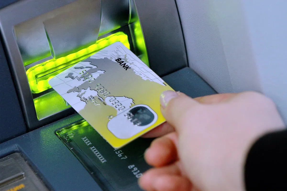 a person puts a debit card into an ATM.