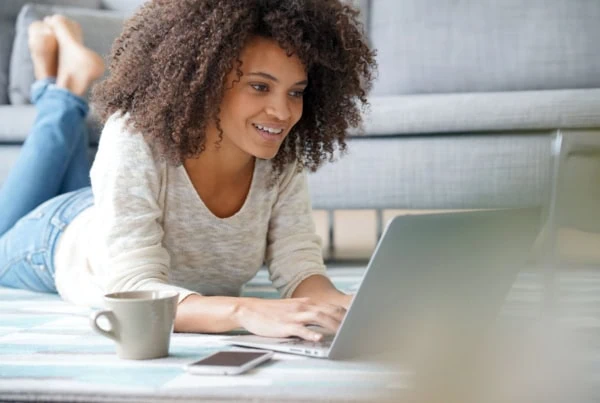 young generation z woman smiles while lying down and looking at her laptop.