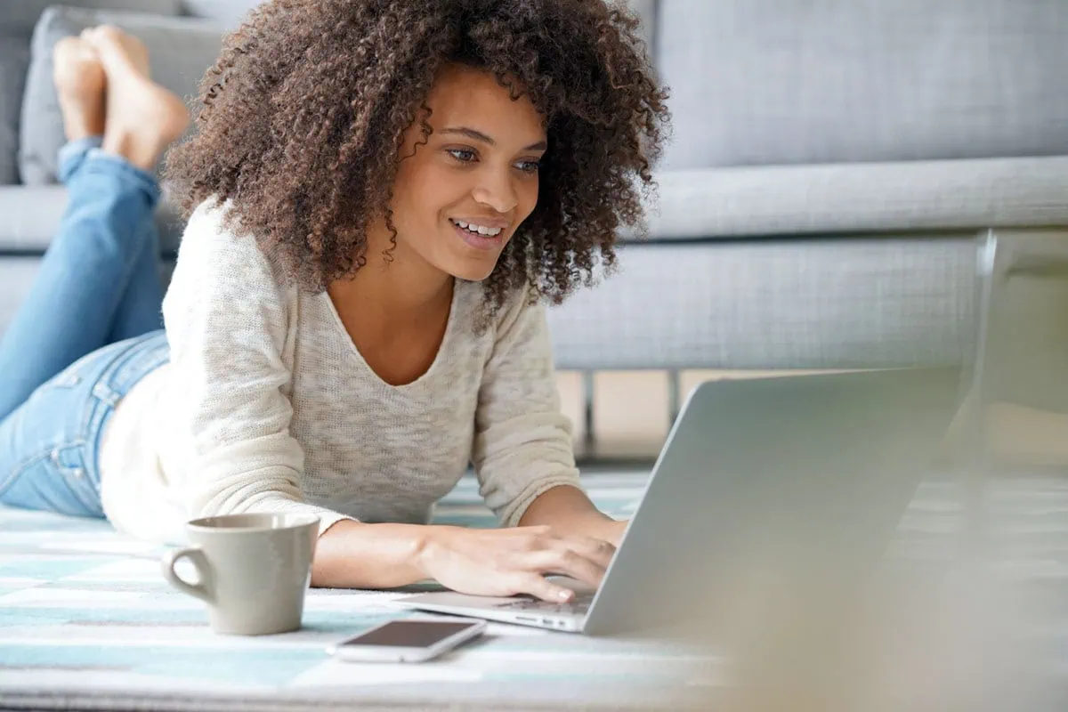 young generation z woman smiles while lying down and looking at her laptop.
