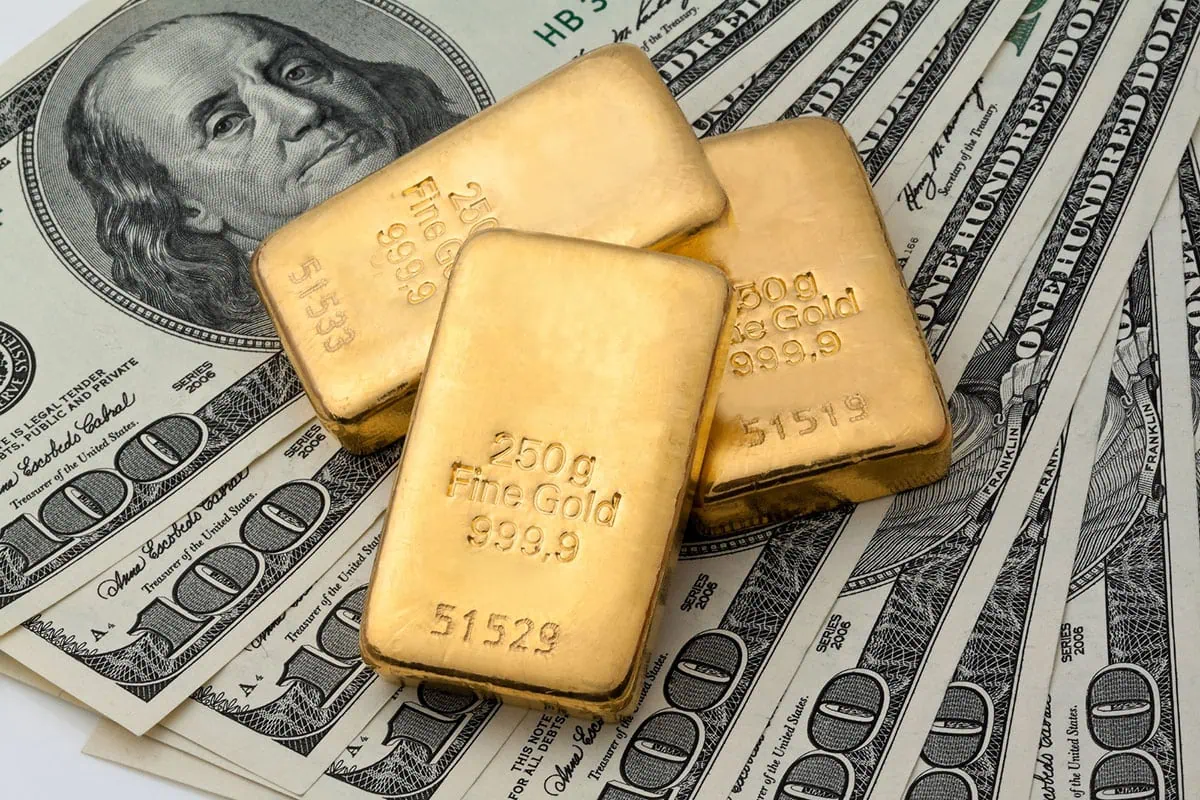 Want to Buy Gold? These Are the 7 Best ETFs for the Job 2 gold bars sit on top of several hundred dollar bills.