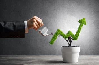 Hand of woman watering small plant in pot shaped like a growth arrow in a chart.