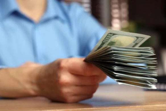 a person holds out a stack of hundred dollar bills.