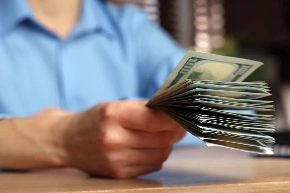 Investing in Her Future: Financial Bat Mitzvah Gifts That Build Success 2 a person holds out a stack of hundred dollar bills.