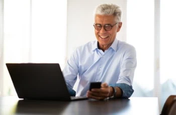 smiling businessman sitting at table with laptop and mobile phone