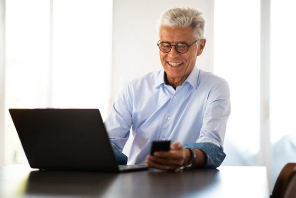 smiling businessman sitting at table with laptop and mobile phone