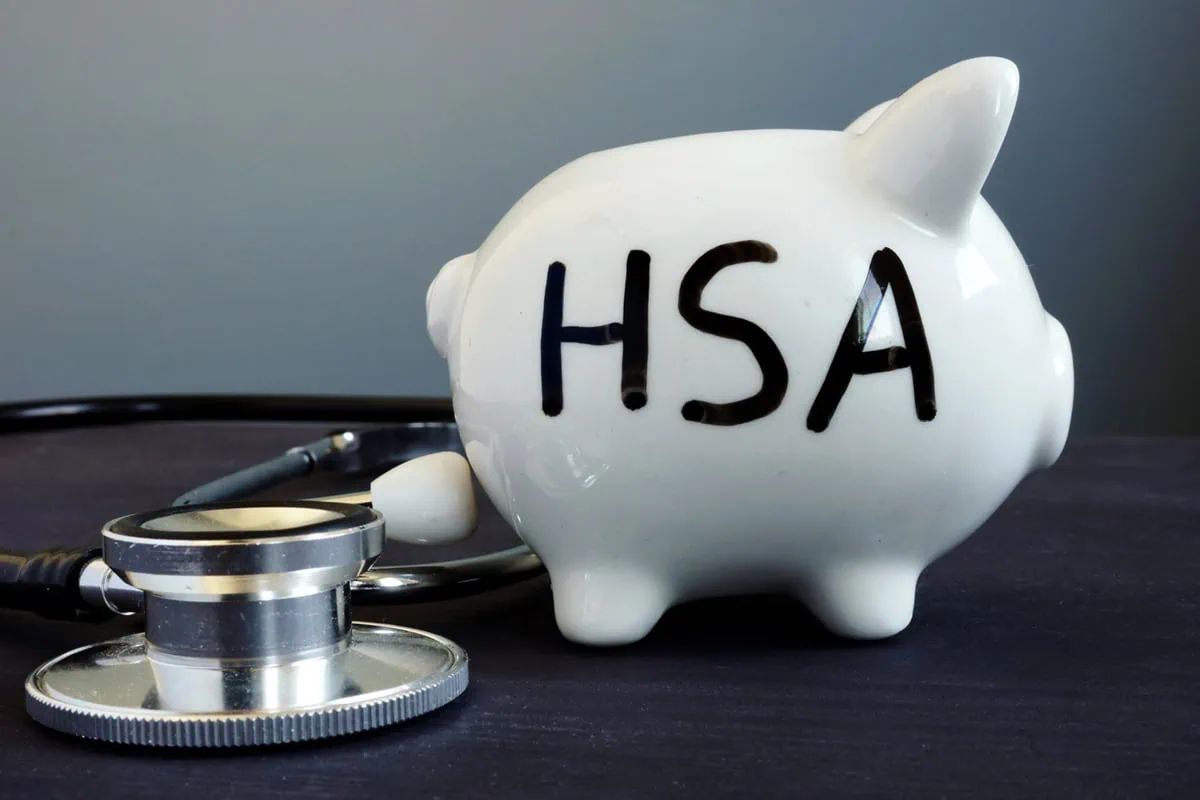 Found a Better HSA? Here’s How to Transfer Your Wealth Without the Headache 2 a piggy bank with the letters H S A on it sits next to a stethoscope.